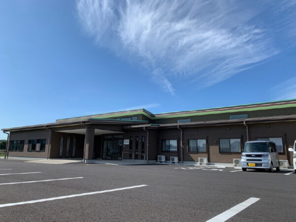 介護施設の建物外観。モダンな平屋建てで、駐車場と玄関が見える。